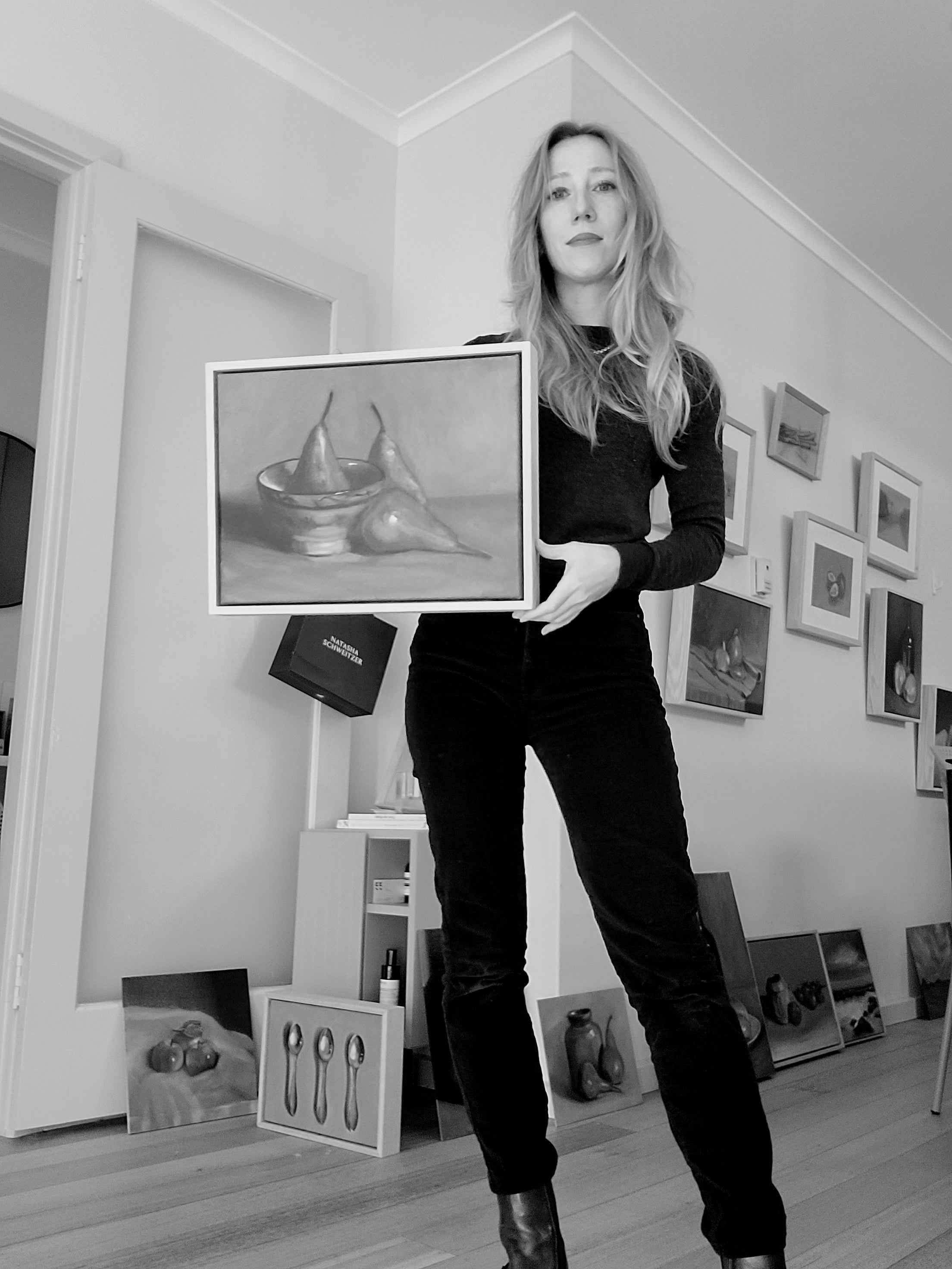 Person holding a framed artwork in an art studio with various artworks on the walls.